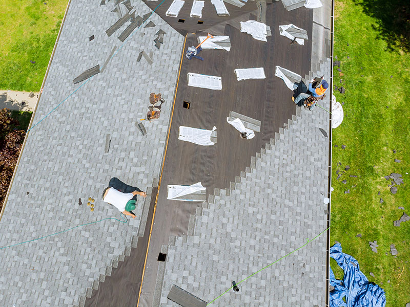 Birds-eye view of workers replacing a residential roof with brand new gray shingles